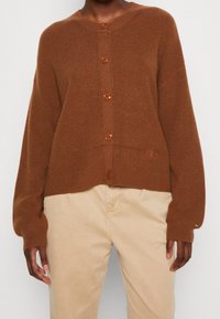 Brauner gerippter Cardigan mit großen braunen Knöpfen und Rundhalsausschnitt, der eine lockere Passform und einen leichten Crop in der Taille aufweist.