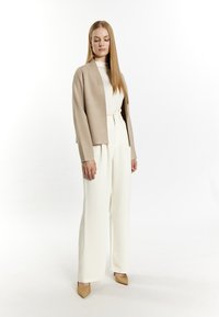 Beige cardigan over een wit topje, gecombineerd met hooggetailleerde witte broeken en beige puntige hakken; soepele texturen en een ontspannen pasvorm.