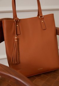 Tandová kabelka z umělé kůže se zlatými detaily a dlouhým třásním. Obsahuje dvojité ucha a má strukturovaný design.