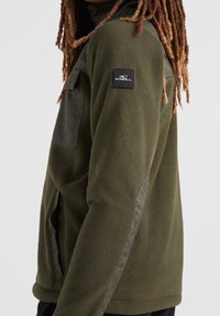 Grøn fleecejakke med nylon detaljer, sidelommer og et logo-patch på ærmet. Har en afslappet pasform og tekstureret overflade.