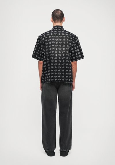 Short-sleeve black shirt with white diamond pattern, relaxed fit, paired with loose black jeans and black shoes, viewed from the back.