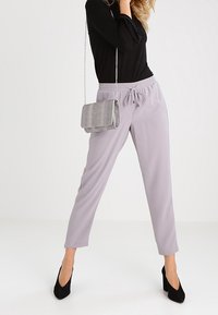 Lys grå tapered bukser med elastisk talje, parret med en sort langærmet top og en struktureret sølv skuldertaske. Sorte højhælede sko.