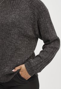 Temno siva pletena pulover s teksturo z ribami, s spuščenimi rameni in dolgimi rokavi. Stranski razporek na robu dodaja podrobnost. Mehek material.