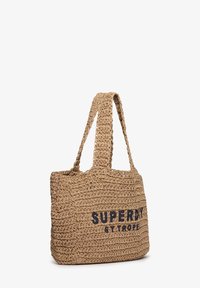 Bolso tote de paja tejida en beige con forma rectangular, con un logo azul marino "SUPERDRY ST TROPE." Asas largas para facilitar su transporte.
