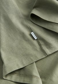 Olive green cotton T-shirt with smooth texture. Features stitched hems and a small label with "jack & jones" near the bottom seam.