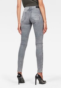 Vaqueros skinny grises de cintura alta, con costuras detalladas, dos bolsillos traseros y una textura suave, combinados con tacones altos negros.