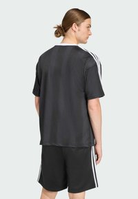 Melnā sporta krekls ar viegliem vertikāliem svītrām, īsām piedurknēm un baltajām akcents ap apkakli un sāniem, apvienots ar melnām šortiem.