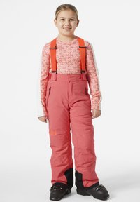 Pantalones de esquí rosas con tirantes naranjas ajustables, acentos negros en los puños y bolsillos laterales con cremallera, llevados sobre una camiseta de manga larga con estampado.