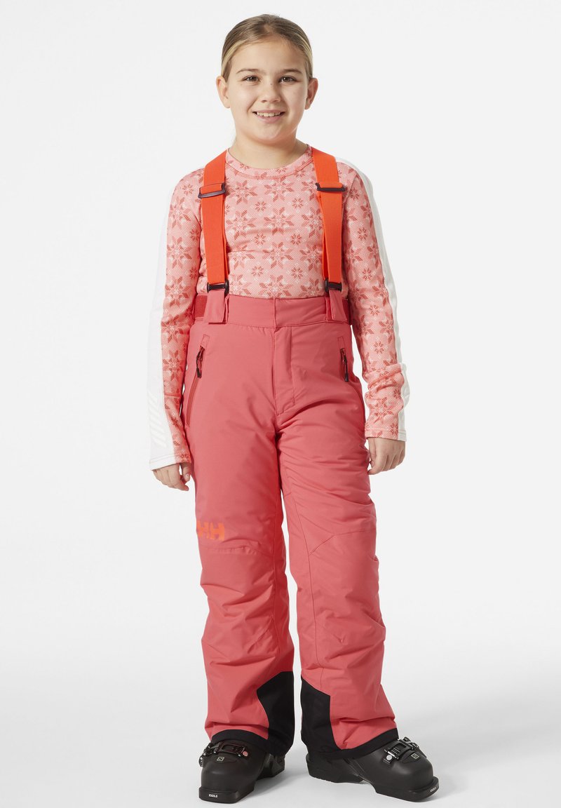 Pantalones de esquí rosas con tirantes naranjas ajustables, acentos negros en los puños y bolsillos laterales con cremallera, llevados sobre una camiseta de manga larga con estampado.