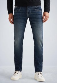 Temno modri jeans s ravnim krojem, ki vsebujejo sprednje žepke in subtilen izbleden design. V kombinaciji z belimi športniki.