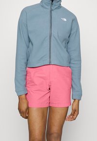 Ljusblå zip-up fleecejacka med hög krage, matchad med rosa shorts. Båda plaggen har en avslappnad design och en mjuk textur.