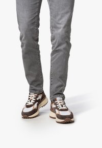 Braun-weiße Sneaker aus einer Mischung von Wildleder und Mesh-Materialien. Masse Sohle und dicke Schnürsenkel; ausgeprägtes Gummiprofil an der Außensohle.