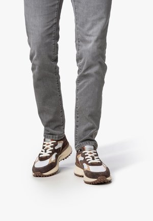 Zapatillas marrones y blancas con una mezcla de materiales de ante y malla. Suela gruesa y cordones gruesos; dibujo de goma prominente en la suela exterior.
