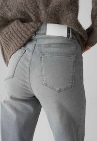 Jeans in denim grigio con un design a vita media, tasche posteriori e una patch in pelle bianca in vita. Texture morbida e taglio aderente.