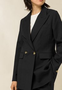 Blazer doppiopetto grigio scuro con bottoni dorati, con due tasche frontali e design con rever a lancia su tessuto strutturato.