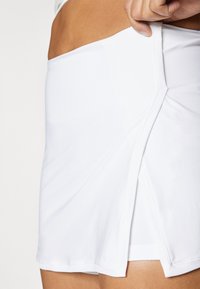 Bela športna krila iz mehke, raztegljive tkanine z bočnim razporkom in gladkimi šivi. Dizajn omogoča lahkotno gibanje in udobje.