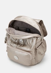 Metallic beige ryggsäck med ett blixtlåsförsett huvudfack, framficka och textilstruktur. Två axelremmar och ett handtag på toppen.