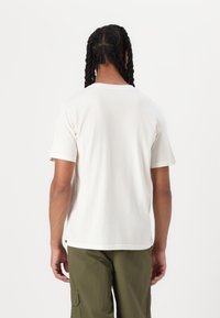 Light cream cotton t-shirt with short sleeves and a round neck, featuring a straight hem and a small logo tag at the lower side.