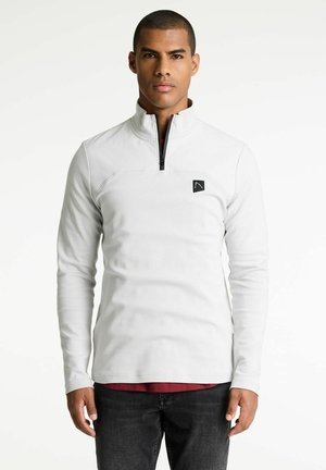 Pull en polyester blanc à manches longues avec une fermeture éclair quart et un patch logo noir sur la poitrine. Il présente une texture lisse et une coupe ajustée.
