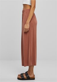 Hnědé culottes širokých nohavic z měkké látky s elastickým pasem, v kombinaci s černými sandály na remínky s korkovými podrážkami.