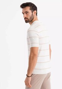 Lyhythihainen, valkoinen neulottu villapaita, jossa on vaaleanbeigejä raitoja. Ribbaa kaula-aukossa ja helmassa, sileä pinta, muotoon ommeltu malli, yhdistetty vaaleisiin housuihin.