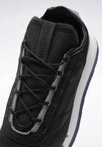 Basket noire Reebok avec lacets élastiques sans nouer, dessus en tissu texturé et semelle blanche avec dessous bleu foncé.