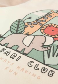 Bawełniana tkanina z kolorową ilustracją szarego słonia, żyrafy i lwa wśród zielonych liści, z tekstem poniżej.