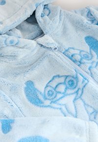 Vêtement en polaire bleu doux avec fermeture éclair et capuche, avec des motifs de voitures cartoon bleu foncé et des pois.