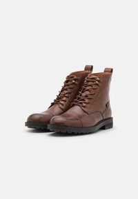 Braune Leder-Stiefeletten mit runden Zehen, Schnürung vorne, Metallösen und strukturierten schwarzen Gummisohlen. Mit Anziehschlaufen gestaltet.