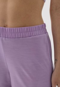 Fioletowe spodenki sportowe o miękkiej, gładkiej fakturze. Posiadają elastyczny pasek w talii i boczne kieszenie. Materiał wydaje się lekki i przewiewny.