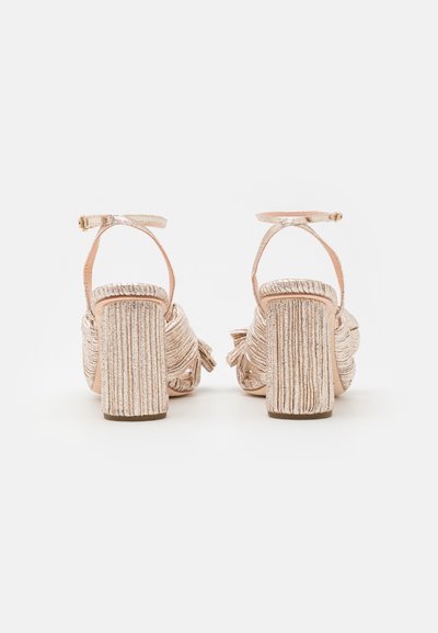 Sandali con tacco a blocco di colore rosa oro metallizzato, dotati di un design frangiato e una cinghia alla caviglia regolabile.
