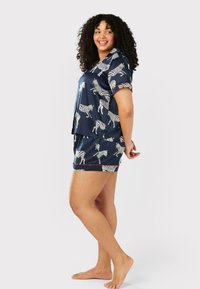 Marinblå pyjamasset med kort ärm och zebramönster, med röda pipade detaljer och lätt tyg. Setet inkluderar en topp och shorts.