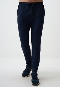Pantalons de survêtement bleu marine avec taille élastique et cordon de serrage ajustable, dotés de poches latérales, coupe fuselée et tissu doux. Associés à des baskets.