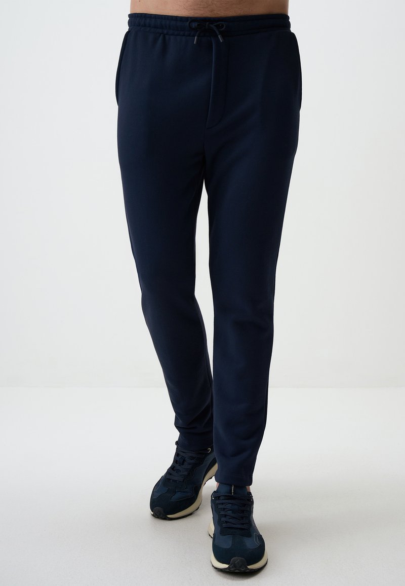 Pantalons de survêtement bleu marine avec taille élastique et cordon de serrage ajustable, dotés de poches latérales, coupe fuselée et tissu doux. Associés à des baskets.