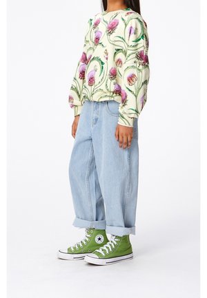 Personne portant un sweat-shirt crème avec un motif de chardon violet, un jean large à revers bleu clair et des baskets montantes Converse vertes.