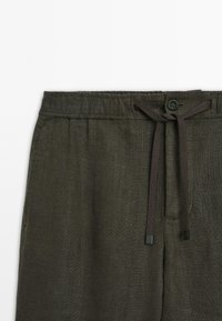 Dark green linen pants with an elastic waistband, front button closure, and a drawstring tie. Features smooth texture and side pockets.