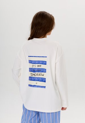 Sweatshirt oversize blanc présentant un design rayé bleu et blanc au dos avec le texte : "Tout va bien. Essaie encore demain."