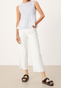 Top peplum bianco in lino, pantaloni bianchi a gamba larga e sandali neri con dettaglio a fibbia. Texture liscia con vestibilità rilassata.