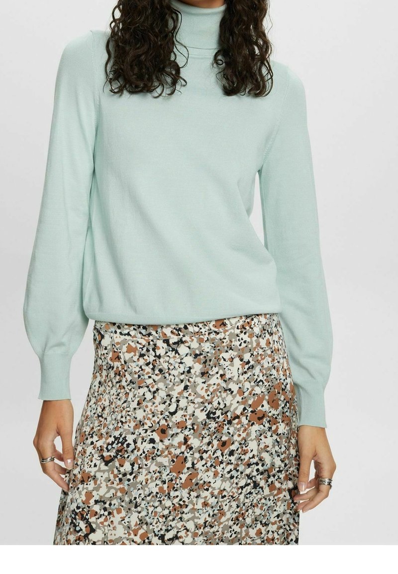 Femme portant un pull à col roulé bleu clair associé à une jupe taille haute à motif floral multicolore.