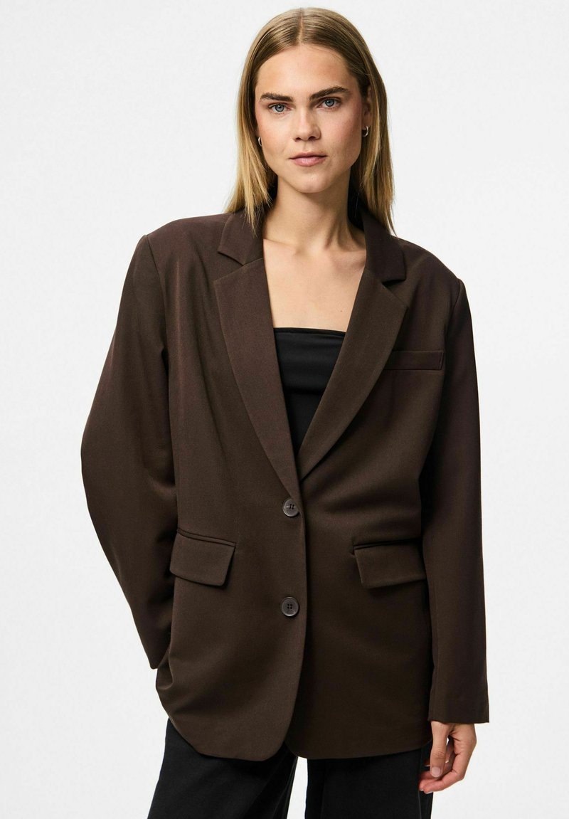 Brūns oversized bleiseris ar izgrieztiem apkaklēm, divām priekšējām kabatām un vienu pogu aizdari. Gluda auduma struktūra ar noformētu siluetu.