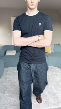 Marinblå kortärmad skjorta med vit kant, parat med mörka jeans. Bruna skor. Ljust soffläge och en gul kudde i bakgrunden.