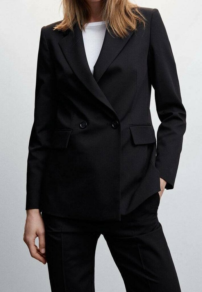 Schwarzer doppelt geknöpfter Blazer mit Reverskragen, zwei vorderen Taschen und taillierter Passform. Über einem weißen Oberteil getragen, kombiniert mit schwarzen Hosen.