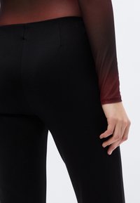 Μαύροι κολάν με λεία υφή, διαθέτοντας ψηλή μέση και διακριτικές ραφές, συνοδευόμενοι από ένα διαφανές τοπ με βαθμιαία αλλαγή χρώματος.