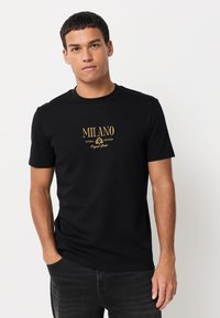 Fekete rövid ujjú pamut póló, arany "MILANO" felirattal a mellkason, klasszikus kerek nyakkivágással.