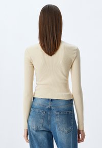 Beige geribbelde langsliepe top met een getailleerd ontwerp, gecombineerd met lichtblauwe high-waisted jeans met twee achterkantzakken en een klassieke snit.