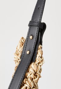 Kudottu olkakassi pellavasta, jossa on musta nahkaremmi ja kultasävyisiä niittejä. Rakenne on pyöreä ja pinnassa on teksturoitu, luonnollinen viimeistely.