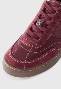 Burgundy sneaker with suede and fabric upper, rubber sole, white stitching accents, and a metal logo on the laces. Rounded toe design.