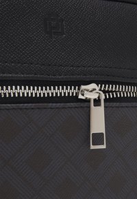 Black textured backpack with a zippered closure; features a silver zipper pull and a dark patterned lower section. Logo embossed on upper part.