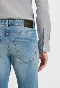 Jean en denim bleu clair avec une texture délavée, comportant deux poches arrière et une étiquette noir avec le logo "BOSS" au niveau de la taille.