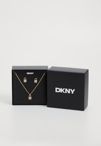 Gouden sieradenset met een hanger in de vorm van een slot en bijpassende oorbellen, verpakt in een zwarte DKNY geschenkdoos met logo.